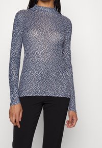 Top a maniche lunghe e colletto alto realizzato in tessuto blu trasparente con un piccolo motivo floreale. Presenta una vestibilità aderente e una superficie testurizzata.