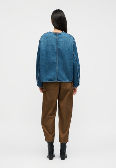 Τζιν πουκάμισο σε μπλε χρώμα με φαρδιά γραμμή, στρογγυλή λαιμόκοψη και εμφανείς ραφές. Συνδυασμένο με καφέ παντελόνι καμπαρντίνας και μαύρα μποτάκια αστραγάλου.