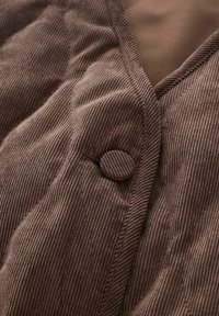 Nahaufnahme von braunem Cordstoff mit einem verdeckten Knopf und sichtbaren Nähdetails.
