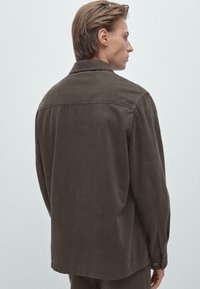 Bruine, textuurshirt met een puntkraag en lange mouwen. Voorzien van knopen op de manchet, een op maat gemaakte rugnaad en een ontspannen pasvorm.