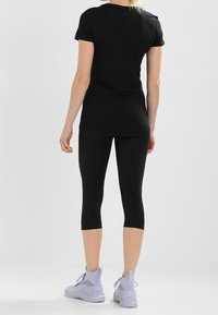 T-shirt noir à manches courtes associée à des leggings noirs mi-mollet et des chaussures de sport gris clair, avec une coupe décontractée et un design minimaliste.