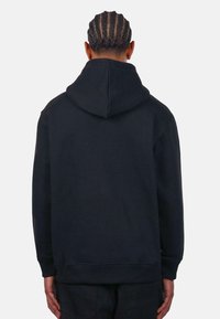 Must häelmust, millel on tagantvaade, reguleeritava kinnisega kapuuts, pikad varrukad ja soonikuga mansetid. Sile kangastekstuuri, ilma nähtavate logode või mustriteta.