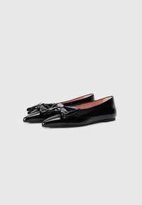 Ballerines en cuir verni noir avec un bout pointu et un détail de nœud central. Texture lisse avec une doublure intérieure rouge contrastante.