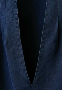 Gros plan sur un tissu denim bleu foncé avec un col en V profond et des coutures visibles le long des bords.