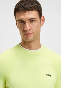 Jasnożółta bluza z teksturowanej tkaniny, z okrągłym dekoltem i małym czarnym logo "BOSS" na lewej piersi.