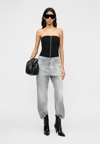 Haut noir sans bretelles avec fermeture éclair à l'avant, jean ample gris clair, bottes noires à bout pointu et lunettes de soleil noires surdimensionnées. Textures lisses partout.