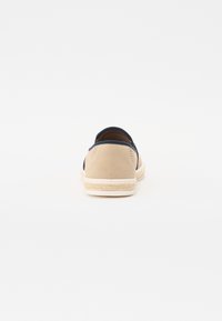 Chaussure beige en daim à enfiler avec des accents bleu marine, semelle en jute tissé et design perforé à l'arrière pour la respirabilité.