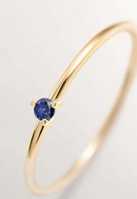 Anillo de oro con una superficie lisa y pulida que cuenta con un zafiro azul redondo engastado en un ajuste de cuatro puntas. Diseño simple y elegante.
