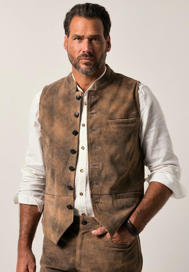 Chaleco sin mangas marrón hecho de un tejido texturizado, con botones negros, un pequeño bolsillo y un cuello alto, usado sobre una camisa blanca.