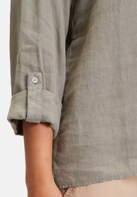 Ljusgrå linne skjortsärmar, uppvikta med knappstängning. Mjuk textur, lös passform, platt sömsdetalj längs fållen.