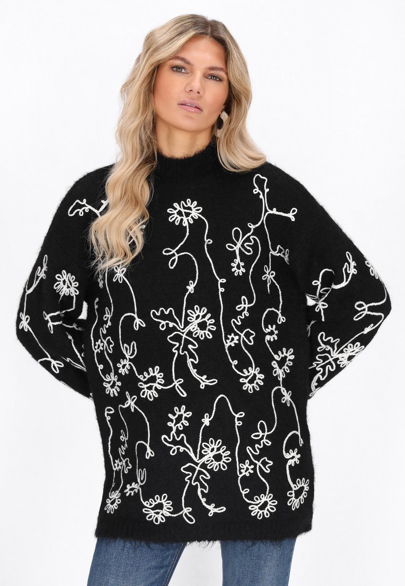 Maglione oversize nero con ricami floreali bianchi, collo alto e orlo a coste. Tessuto morbido e vestibilità rilassata.