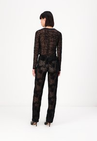 Zwarte doorzichtige lange mouw top met bloemende borduursels, gecombineerd met zwarte kantbroeken met soortgelijke bloemmotieven en stiletto hakken.