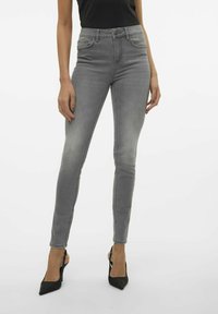 Jeans skinny grises con cintura alta, diseño de cinco bolsillos, desvanecimiento sutil y una textura de mezclilla suave, combinados con tacones negros de punta afilada.