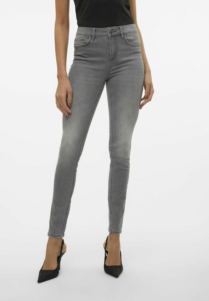 Jeans skinny grises con cintura alta, diseño de cinco bolsillos, desvanecimiento sutil y una textura de mezclilla suave, combinados con tacones negros de punta afilada.