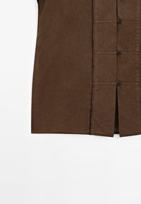Bruine linnen overhemd met een rechte snit, knoopsluiting en een kleine split aan de onderkant voor extra detail. Eenvoudig en minimalistisch ontwerp.