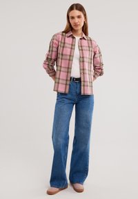 Camicia button-up a quadretti rosa e verdi, in misto cotone, maniche lunghe. Abbinata a jeans in denim blu a gamba larga e alta vita e scarpe rosa chiaro.