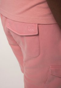 Pantalons de jogging en coton rose avec une poche patch et un logo discret. Le tissu a une texture lisse avec une finition légèrement délavée.