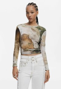 Langarmtop met een abstract patroon in aardetinten, voorzien van een getailleerd ontwerp en een cropped lengte, gecombineerd met hoge taille witte jeans.
