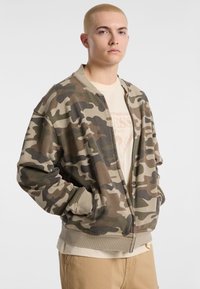 Camouflage bomberjack in aardse tinten, met een ritsluiting, ribgebreide manchetten en zijzakken. Gemaakt van zachte, textuurstof.