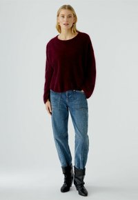 Bordeaux mohair trui met lange mouwen, gecombineerd met blauwe denim jeans en zwarte enkellaarsjes. Zachte textuur en een relaxte pasvorm.
