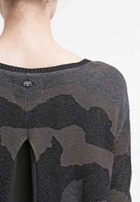 Schwarz und grauer Strickpullover mit einem subtilen Camouflage-Muster, weitem gerippten Ausschnitt und einem Ausschnitt auf dem Rücken. Markentag sichtbar am Hals.