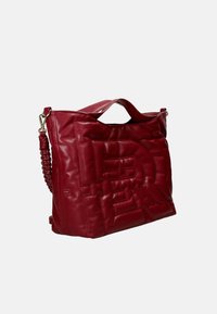 Borsa in pelle rossa con una texture trapuntata, caratterizzata da un logo in rilievo prominente, manico corto e dettagli con tracolla intrecciata.
