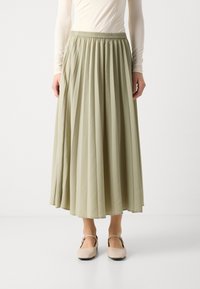 Plisserte midiskjørt i lysegrønn, med elastisk liv. Kombinert med beige, lukkede sko med stropp over ankelen.