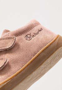 Roze nubucklederen schoen met een gestructureerd oppervlak, voorzien van een klittenbandsluiting en een rubberen zool. Logo in reliëf op de zijkant, lichte goudkleurige glansaccenten.