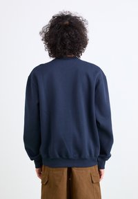 Navy blue sweatshirt made of cotton, featuring a crew neck, ribbed cuffs, and hem. The back is plain with no patterns or logos.