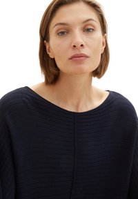 Marineblaues, strukturiertes Strickoberteil mit weitem Ausschnitt und kurzen Ärmeln. Vertikal gerippte Gestaltung und eine zentrale Nahtdetails.