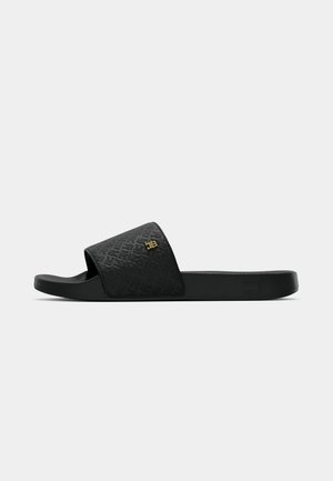 Sandal nera senza lacci con una fascia testurizzata e un piccolo logo dorato su sfondo bianco.