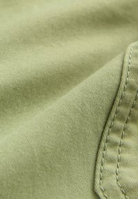 Tissu vert clair à la texture lisse, présentant une vue en gros plan de la couture le long du bord. Des motifs subtils peuvent être visibles dans le tissage.