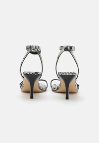 Sandales à talons hauts avec un motif en serpent noir et blanc, dotées de brides ajustables à la cheville et de talons stilettos fins. Semelle plate et design à bout ouvert.