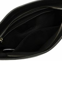 Black leather bag interior with multiple pockets, smooth texture, and gold-tone zipper detail. Lined with black fabric for contrast.