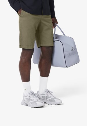 Sac de sport gris clair avec des accents perforés, associé à un short beige et des baskets gris clair. Accompagné de chaussettes blanches.