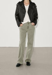 Svart läderbikerjacka, vit V-ringad t-shirt, ljusgröna raka jeans och svarta skor med rund tå. Minimalistisk design.