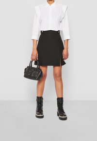 Valkoinen paita röyhelöisillä harteilla, musta minihame sivuhalkiolla, musta niiteillä koristeltu käsilaukku ja mustat nauhalliset saappaat paksulla pohjalla.