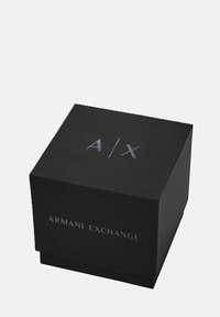 Musta ristkülikuline kast, millel on matt viimistlus, esiküljel hõbedaste kirjadega "A/X" ja "ARMANI EXCHANGE". Kasti kaas on alusega samal tasandil.