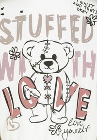 Witte T-shirt met een graphic van een gestikt teddybeer met roze accenten, omringd door tekst, bloemen en harten, dat een boodschap van zelfliefde overbrengt.