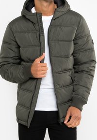 Zielona kurtka puchowa w kolorze oliwkowym z kapturem, z poziomym przeszyciem, zamkiem błyskawicznym i ściągaczami przy mankietach. Wykonana z lekkiego materiału, z funkcjonalnymi kieszeniami.