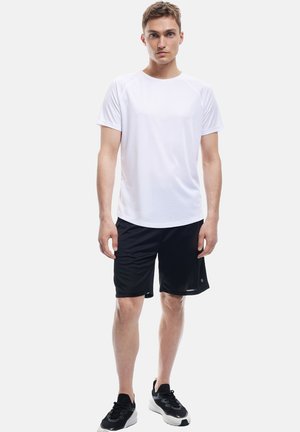 White short-sleeve athletic shirt and black shorts. Shirt has a crew neck; shorts are knee-length with a smooth texture. Black sneakers complete the outfit.