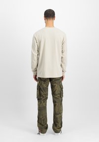 Beiges Langarmhemd aus weichem Stoff, kombiniert mit grünen Cargohosen im Camouflage-Design mit mehreren Taschen und verjüngten Bündchen.