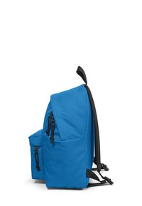 Mochila azul con bolsillo delantero, tiradores de cremallera negros, bolsillo lateral, correas acolchadas negras para los hombros y bucle de transporte, mostrada de lado sobre fondo blanco.