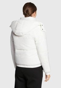 Giacca a vento bianca con cappuccio, polsini elasticizzati e orlo inferiore. Presenta una texture trapuntata e dettagli con bottoni a pressione sul colletto.