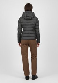 Graue gesteppte Jacke mit Kapuze, Steppmuster und elastischen Bündchen. Kombiniert mit brauner Cargohose mit Seitentaschen und schwarzen Schuhen.
