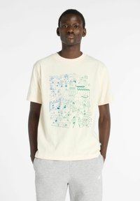 T-shirt en coton crème avec un design graphique bleu et vert représentant diverses figures et scènes athlétiques. Coupe décontractée avec des manches courtes.
