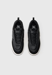 O pereche de sneakers din piele texturată neagră cu talonase albe groase și cu marca "Just Cavalli" pe limbi și pe tălpi.