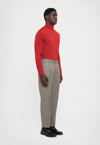Red turtleneck sweater paired with gray plaid trousers and black shoes. The outfit features fitted designs and textured materials.