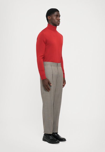 Rød turtleneck sweater parret med grå ternede bukser og sorte sko. Outfittet har tætsiddende designs og teksturerede materialer.