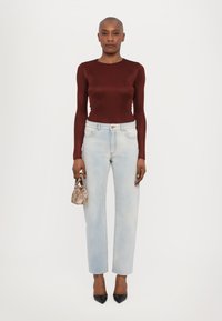 Bordeauxfarbene Langarm-Bluse, hellblaue, gerade geschnittene Jeans, schwarze spitze Absätze, Halten einer gemusterten Mini-Handtasche. Glatte Textur, figurbetontes Design.